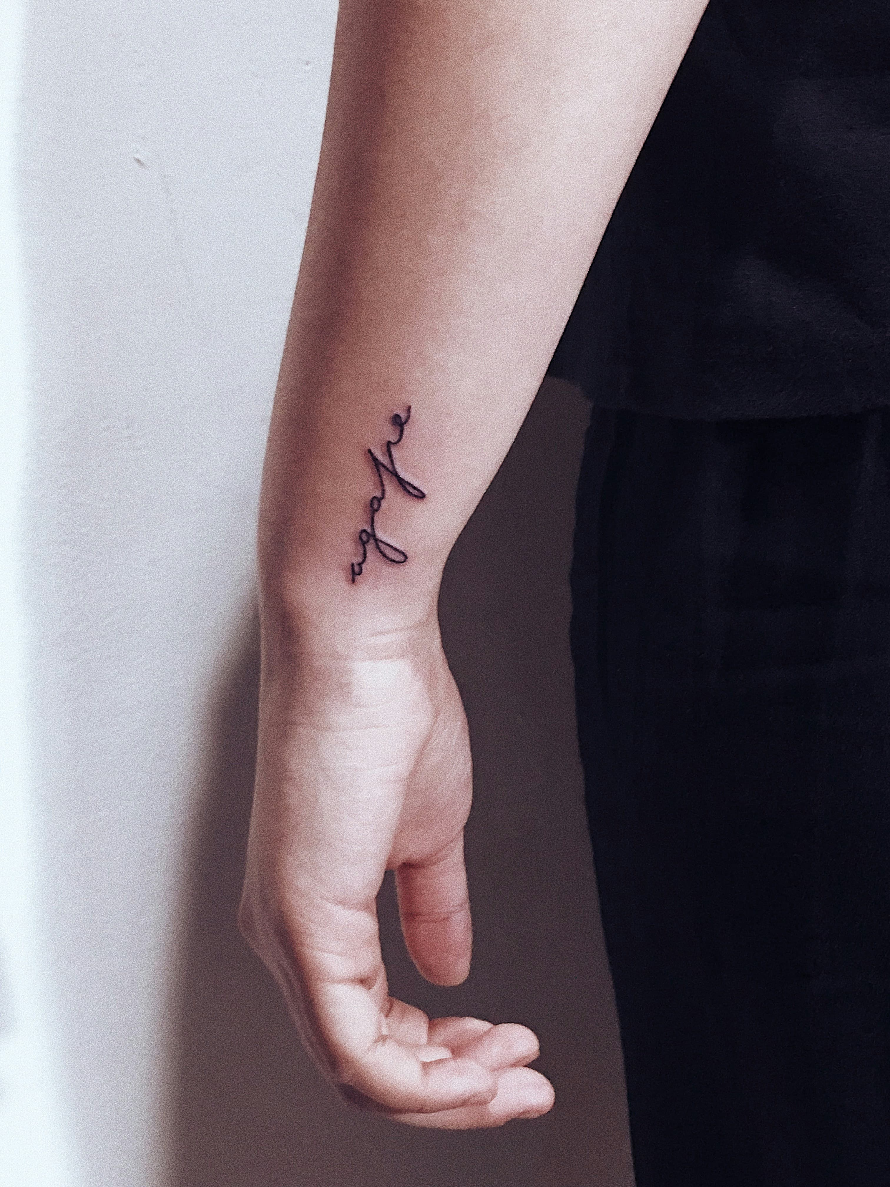 Pequeño tatuaje de escritura fine line en la muñeca