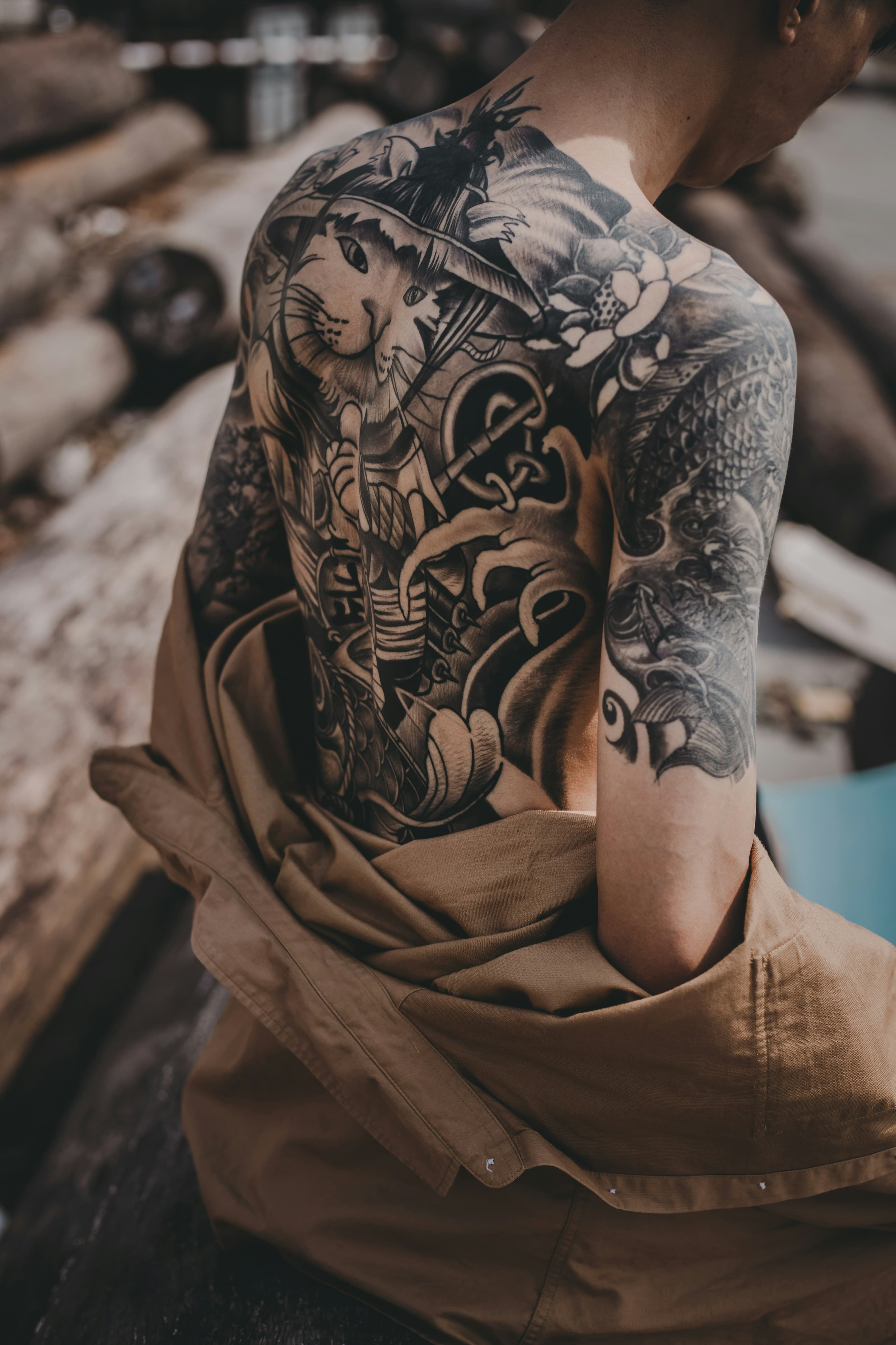 Espalda completa con tatuaje blackwork, cubierta a medias por una chaqueta de lienzo